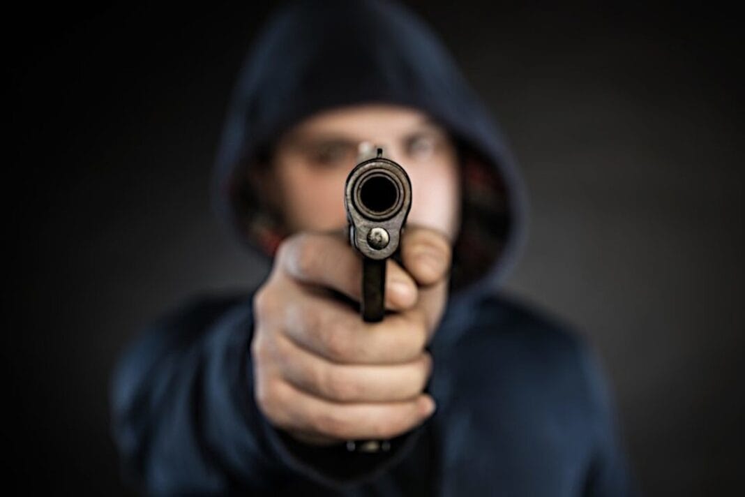 Personne masquée pointant une arme à feu directement vers la caméra.