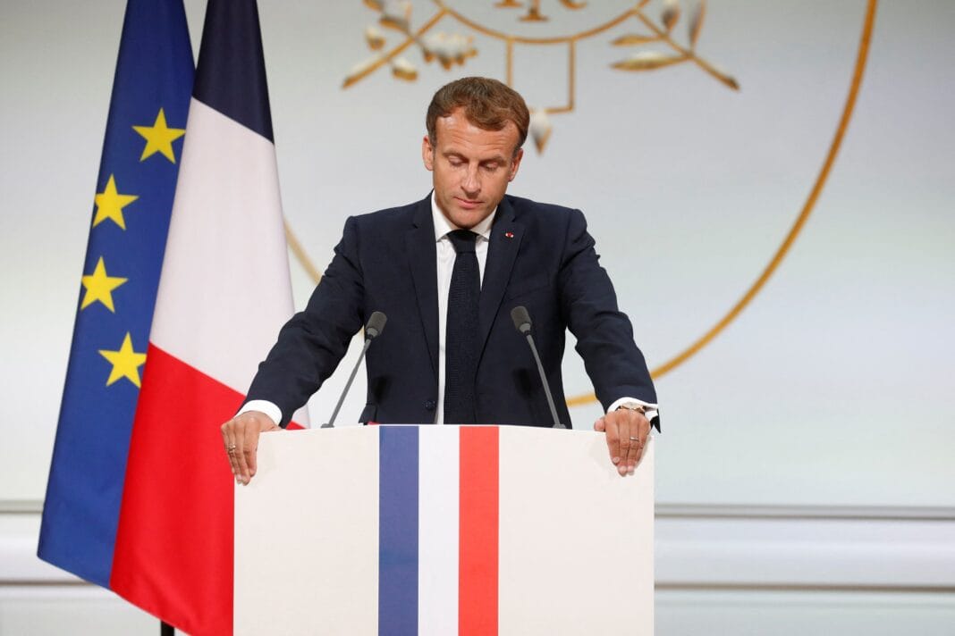 Emmanuel Macron parle lors d'une conférence avec drapeaux français et européens.