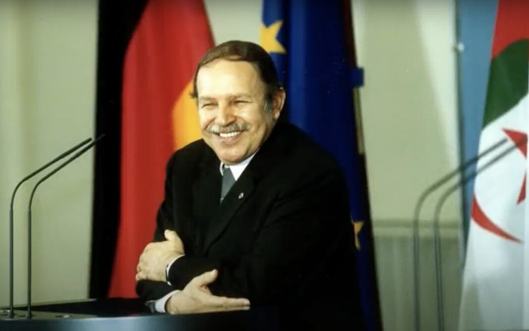Bouteflika symboles des occasions manquées de l’Algérie Bouteflika souriant avec drapeaux algérien, européen et allemand en arrière-plan.