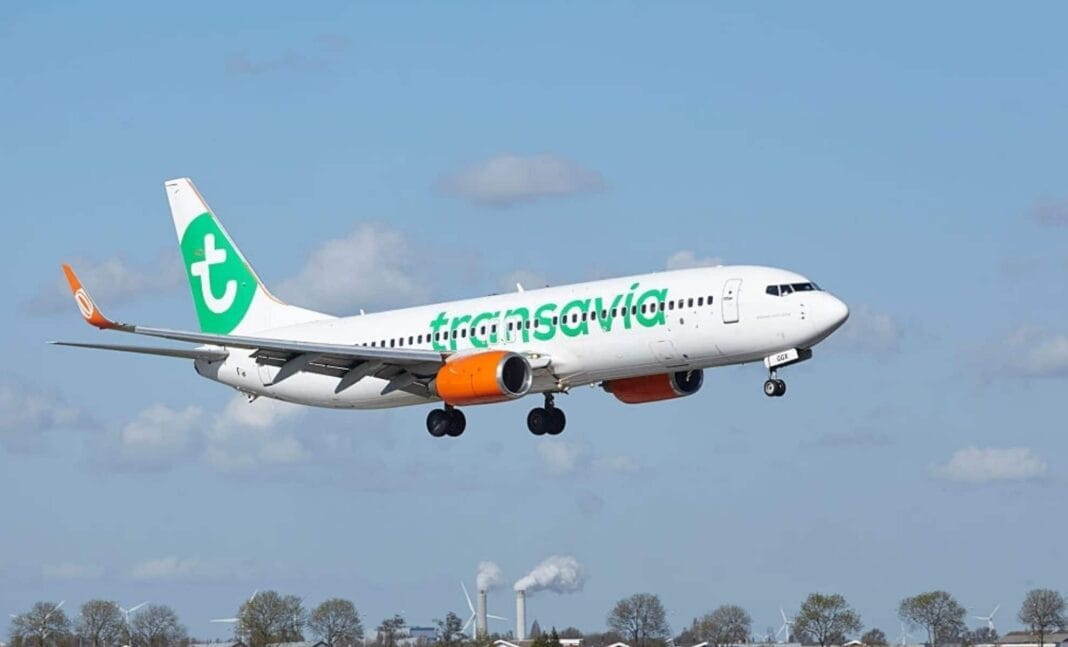 Avion Transavia blanc avec logo vert en vol dans le ciel bleu.