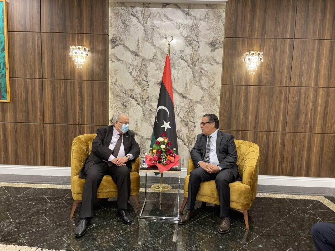 Conférence sur la stabilité de la Libye : Lamamra à Tripoli ce jeudi Deux hommes discutent lors d'une conférence en Libye avec drapeau national en arrière-plan.