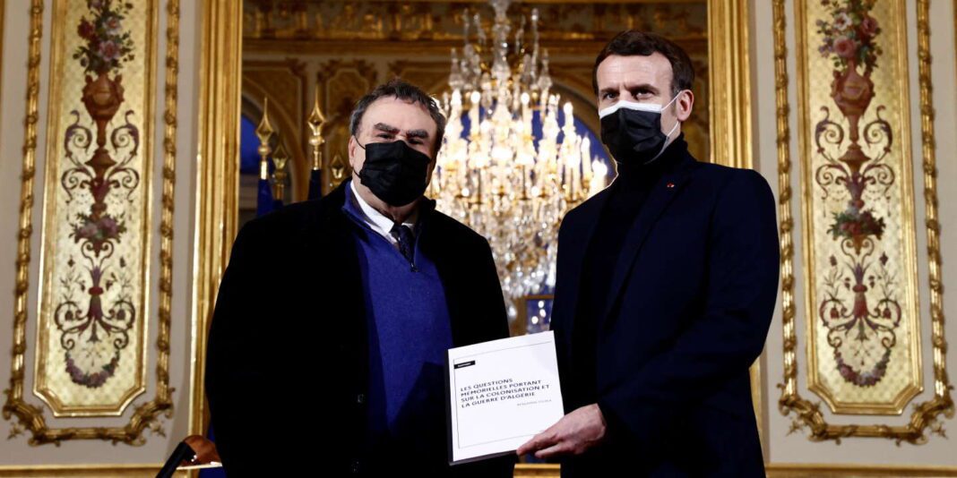« En Algérie, la polémique mémorielle cherche à masquer l’isolement et la fragilité d’un régime » Deux hommes en costume noir avec masques, échangeant un document dans un lieu élégant.