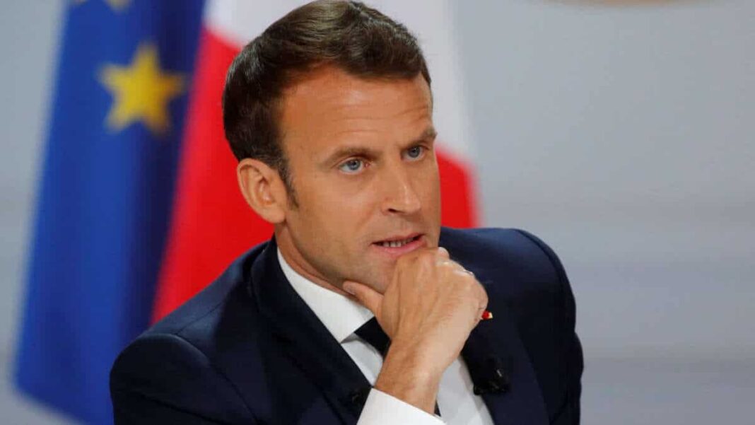 Les contours de l’arrivée prochaine d’Emmanuel Macron en Algérie Emmanuel Macron en interview, fond avec drapeaux français et européen.