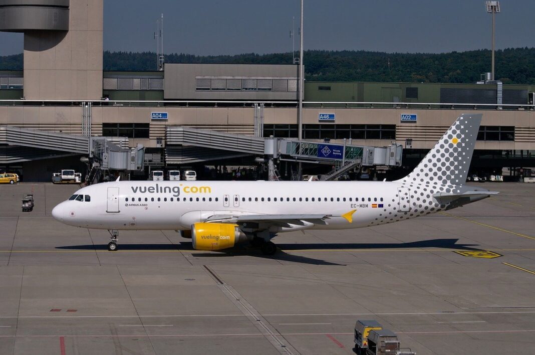 Vols Paris – Alger : Voici les prix de Vueling pour février 2023 Avion Vueling stationné à l'aéroport avec terminal en arrière-plan.
