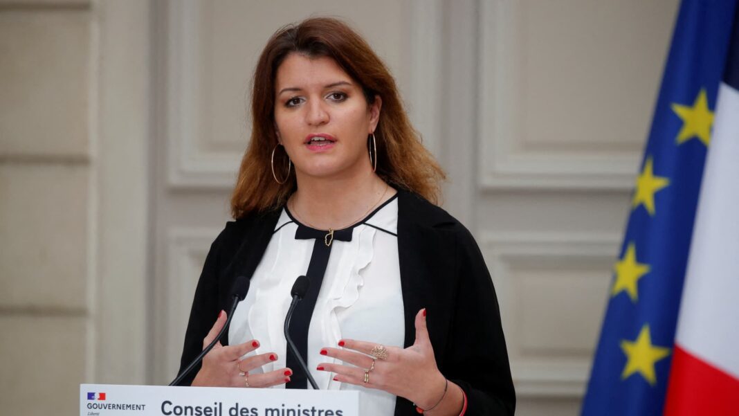 Responsable française critique associations musulm Femme française lors d'une déclaration officielle avec drapeau européen en arrière-plan.