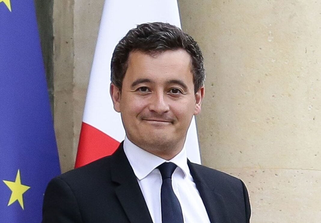 Darmanin : Ceux qui veulent rester en France doivent parler couramment sa langue (vidéo) Homme en costume avec drapeaux France et UE en arrière-plan.