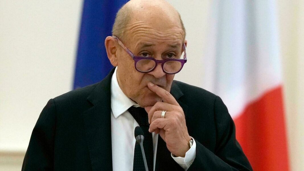 Homme politique pensif avec lunettes, en costume noir, lors d'une réunion officielle.