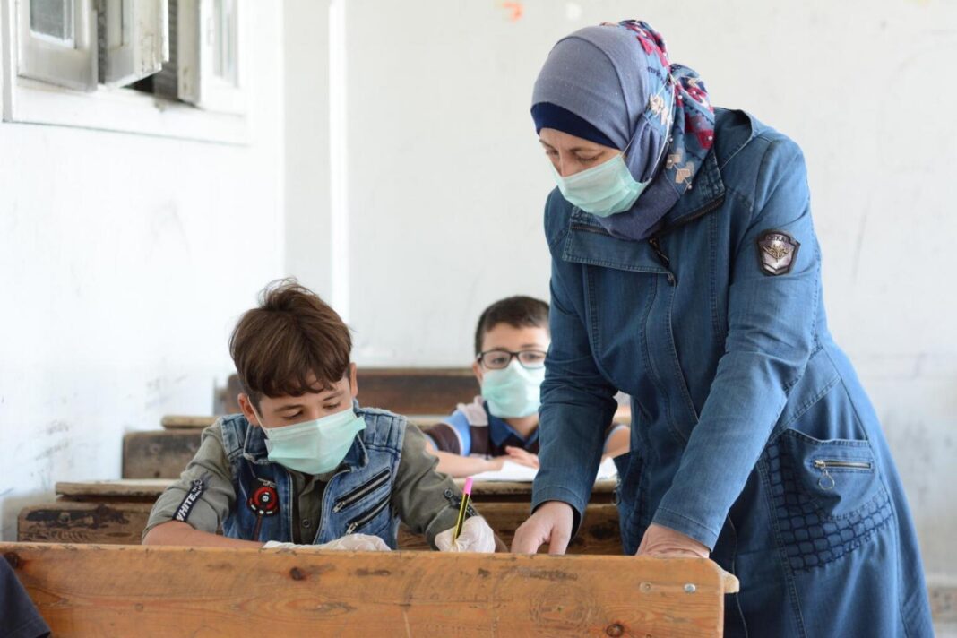 Rentrée scolaire : pourquoi ça traîne ? Enseignante aidant des élèves à l'école avec masques faciaux.