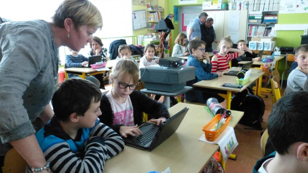Classe d'élèves en salle de technologie Enseignante aidant des élèves à utiliser un ordinateur en classe.