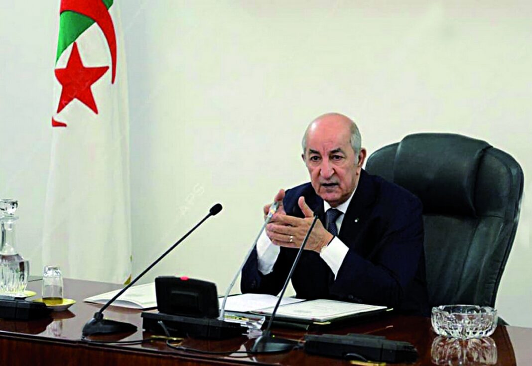Importation des véhicules neufs : Tebboune ordonne la publication… Homme politique algérien lors d'une réunion officielle avec drapeau national en arrière-plan.