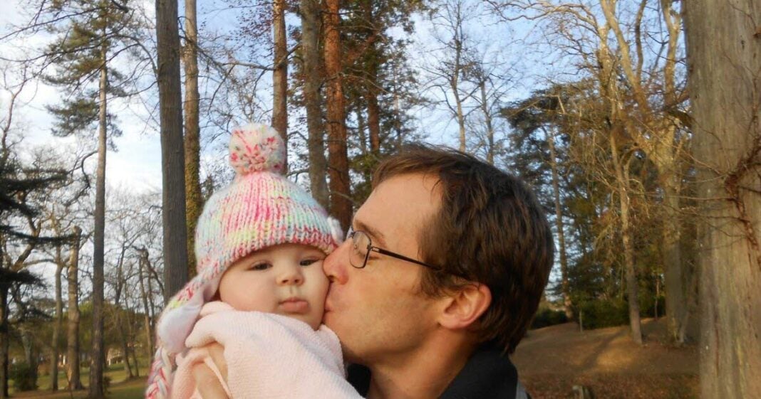 Père embrassant sa fille dans un parc enneigé en hiver.