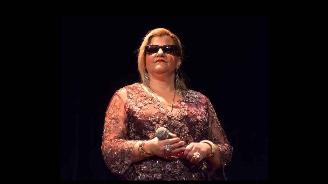 Naima Dziriya portant des lunettes de soleil et tenant un micro sur scène.
