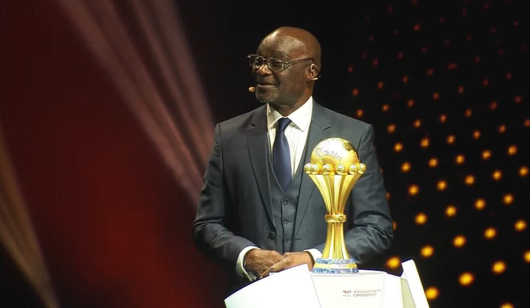 Algérie-Cameroun : « Si moi même j’avais joué avec mes 70 ans, le score allait être plus grave» dixit Roger Milla Homme en costume avec trophée de football sur scène.
