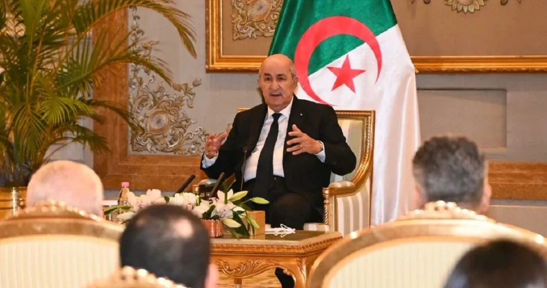 Tebboune lors d'une réunion officielle Président Tebboune parlant lors d'une réunion avec drapeau algérien en arrière-plan.