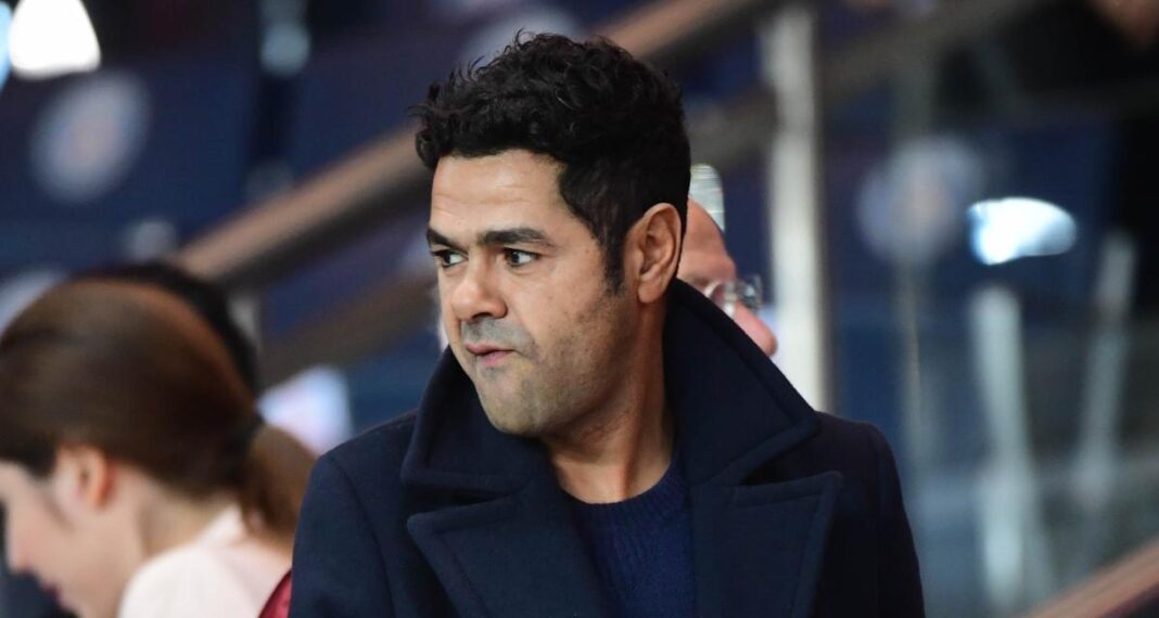 Jamel Debbouze observant un match de football avec concentration.