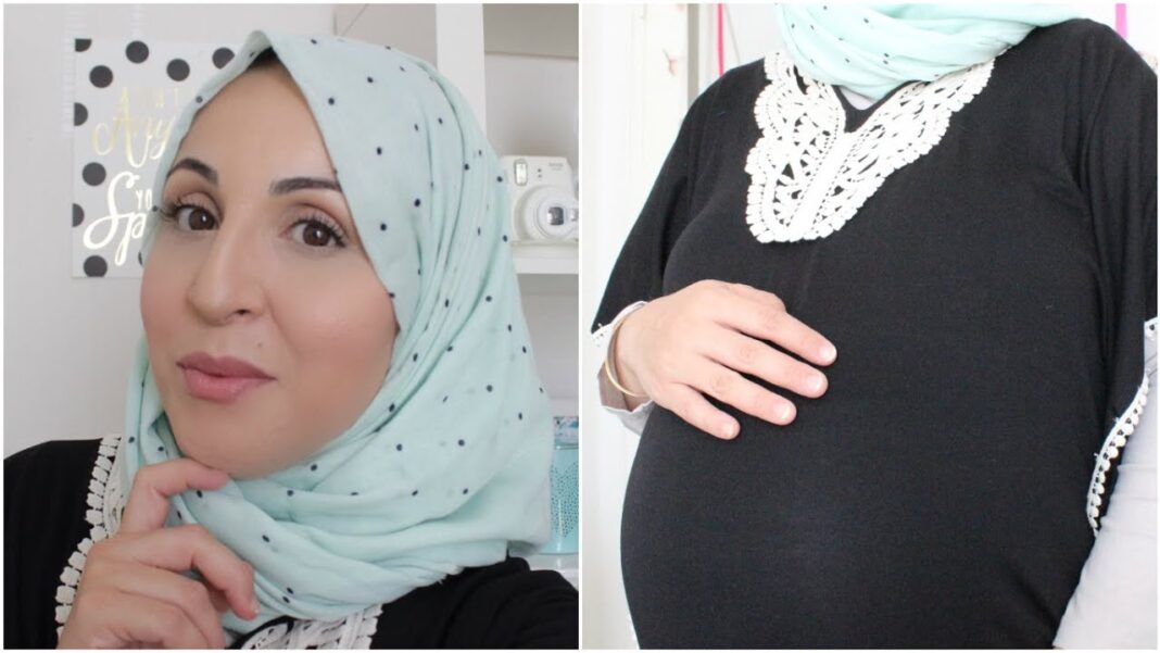 Femme enceinte avec hijab bleu clair, visage souriant, dans un intérieur moderne.