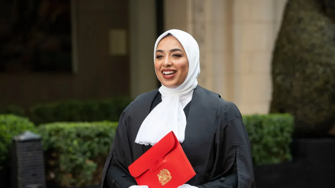 Une avocate voilée nommée conseillère de la reine d’Angleterre Avocate voilée souriante portant un sac rouge avec un symbole doré.