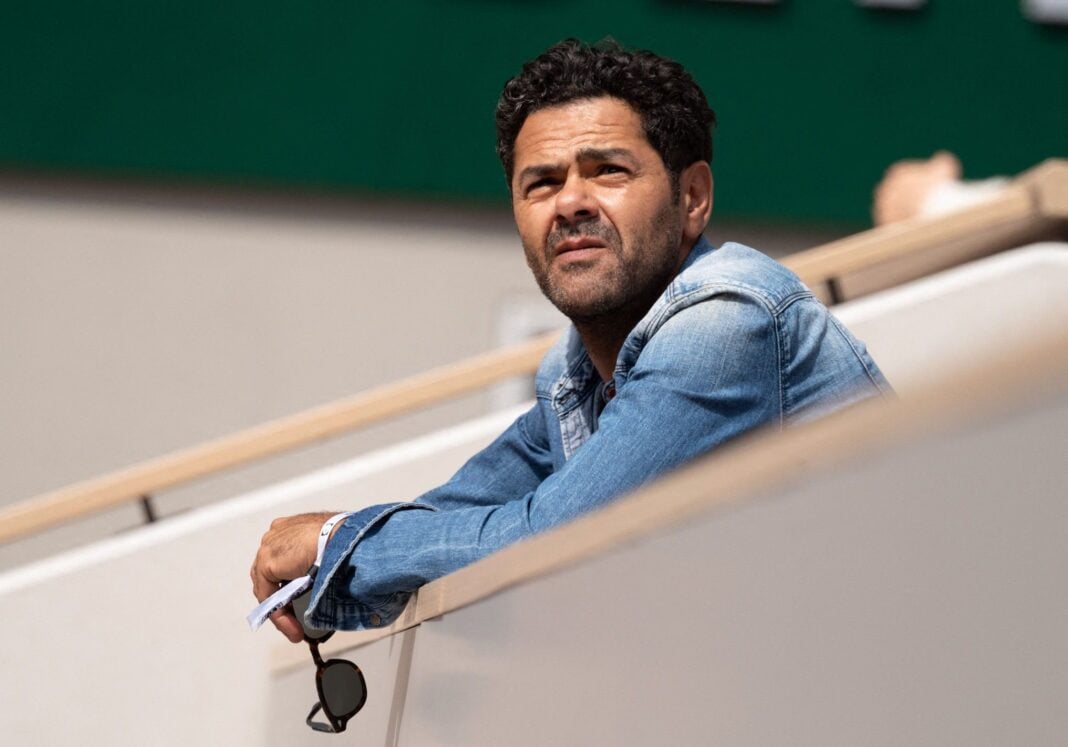 Affaire Gassama : le marocain Jamel Debouze accusé de… Homme méditant dans un stade, regard pensif, ambiance sportive.