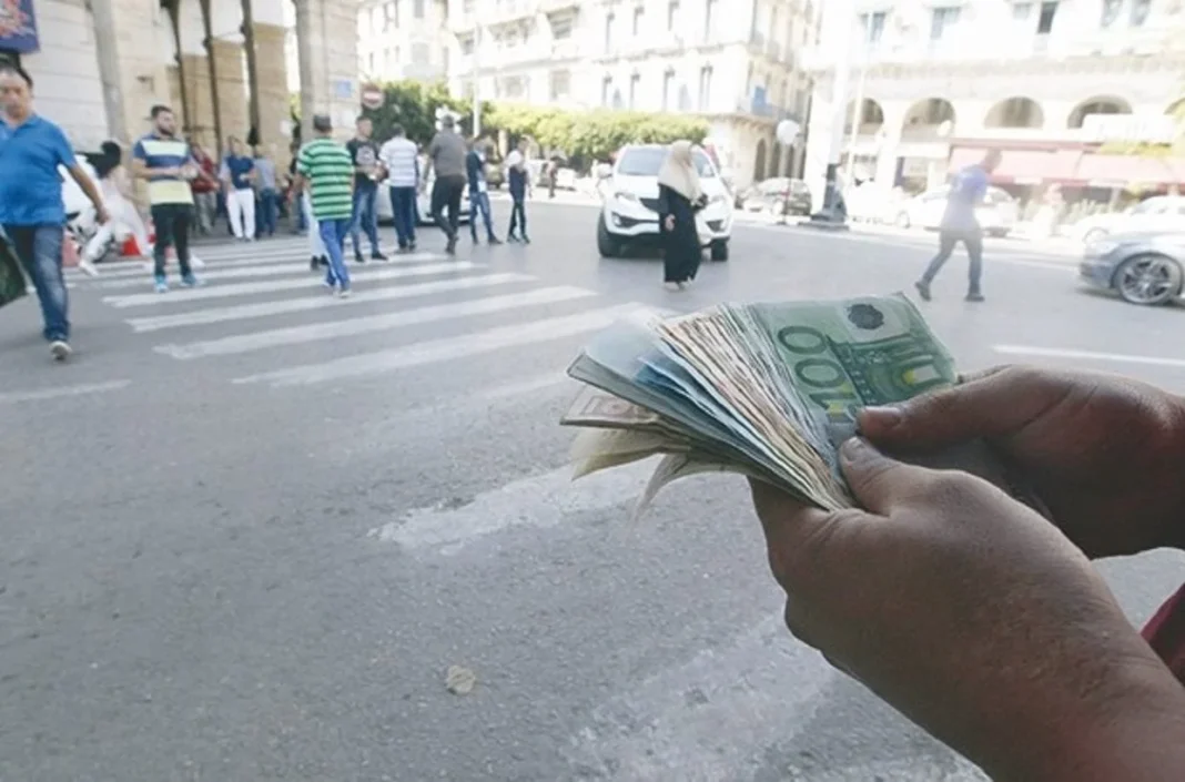 Main tenant des billets de banque face à une rue animée en Algérie.