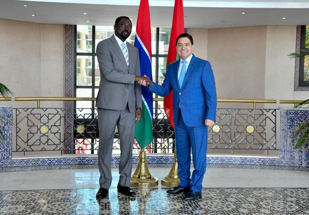 Vers l’ouverture d’un « poste diplomatique » du Maroc en Gambie Deux hommes en costume se serrent la main devant les drapeaux du Maroc et de la Gambie.