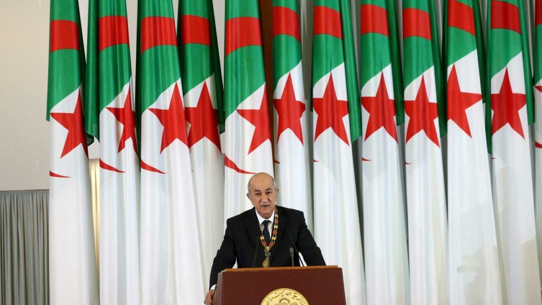 Tebboune devant des drapeaux algériens lors d'une cérémonie officielle.