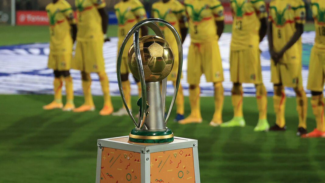 CHAN 2023 en Algérie : la date officielle du tournoi connue ! Trophée de la CAN 2023 avec équipe en arrière-plan.