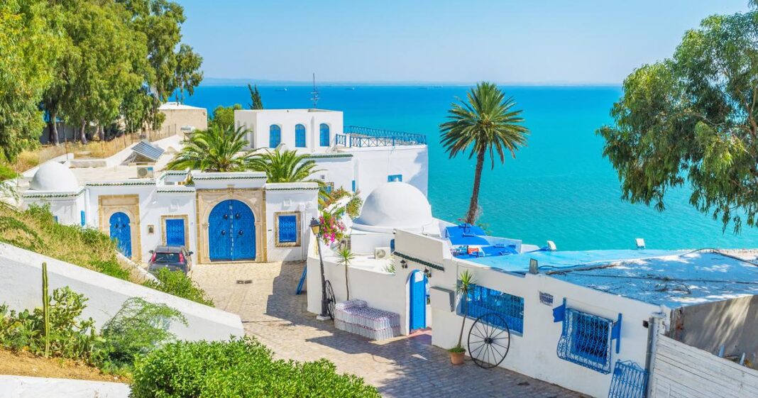 Algérie : les prix des hôtels tunisiens flambent déjà Vue pittoresque d'une ville côtière tunisienne avec bâtiments blancs et mer bleue.