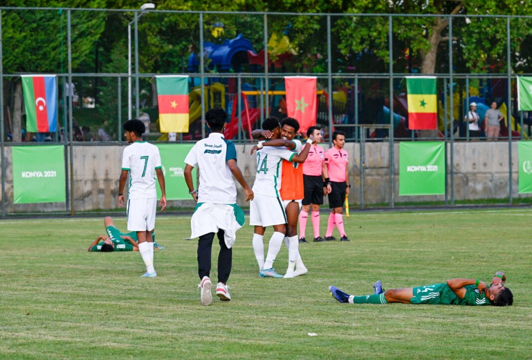 Jeux islamiques : malgré son infériorité numérique, l’Arabie saoudite a éliminé l’équipe d’Algérie en demi-finale sur un score de 2-1 Joueurs de football en action lors des Jeux islamiques avec drapeaux africains en arrière-plan.