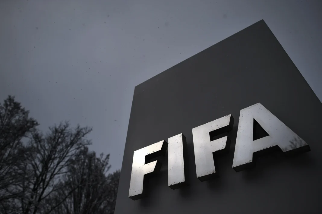 Classement FIFA : l’Algérie dépasse le Cameroun, le Maroc reste fixe Logo de la FIFA sur un panneau en extérieur, ciel nuageux.