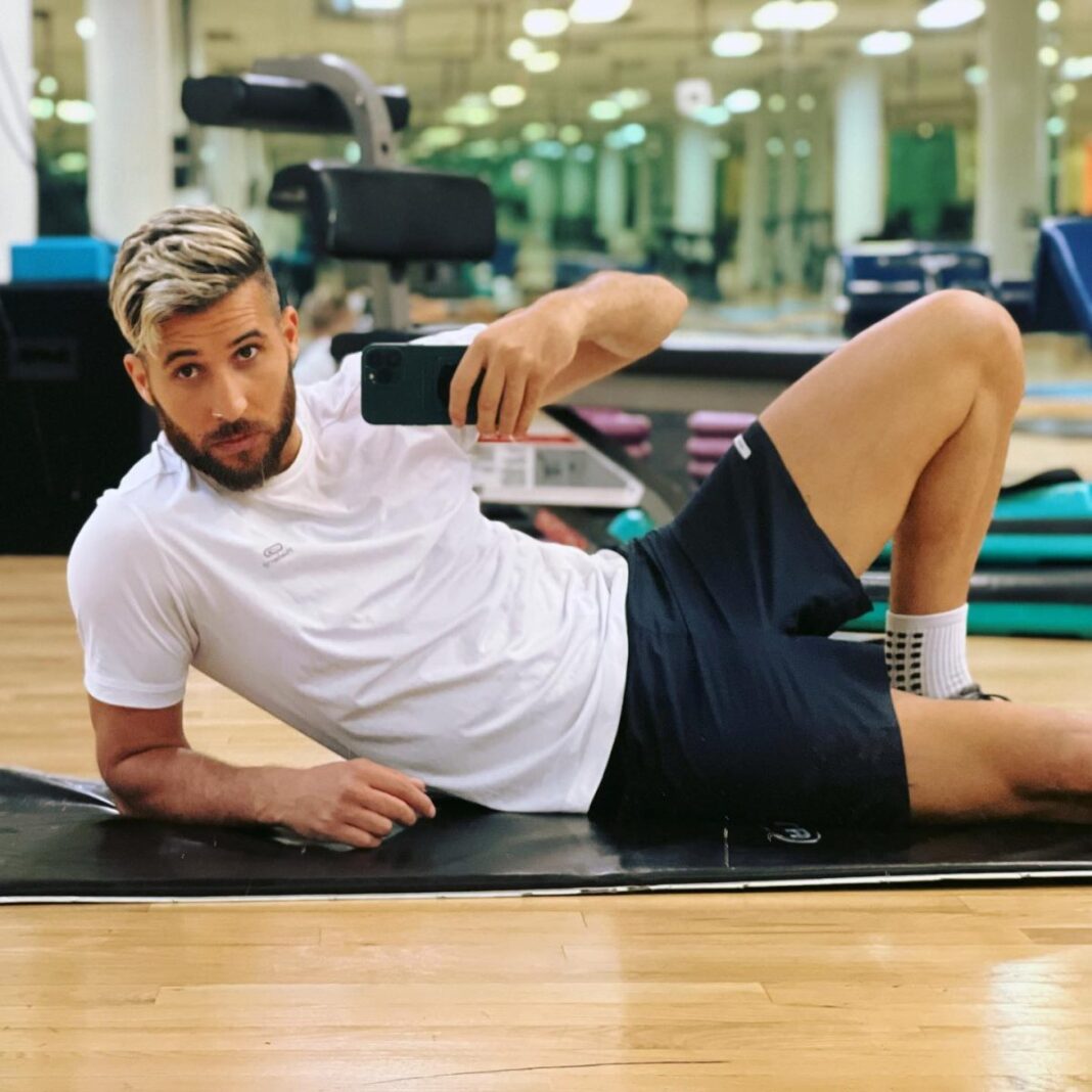 Fayçal Mignon tacle sévèrement Macron Homme prenant un selfie en faisant du sport dans une salle de gym moderne.