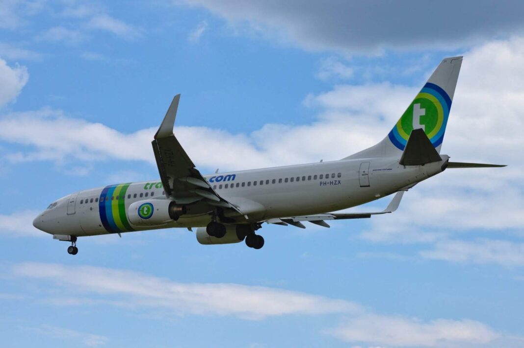 Avion commercial en vol avec logo vert et bleu contre ciel bleu.