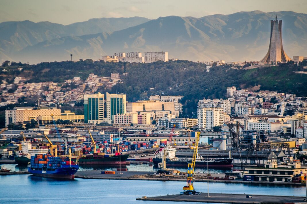 Algérie Ferries : Première traversée vers Dakar effectuée Vue panoramique du port d'Alger avec bâtiments et montagnes en arrière-plan.