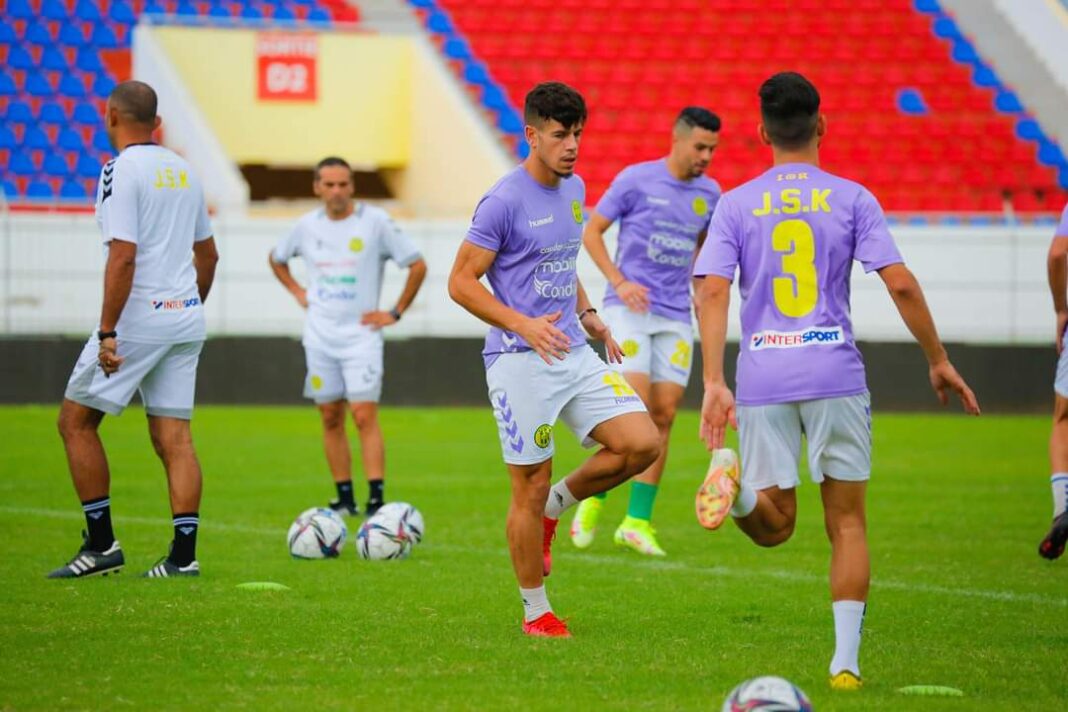 Joueurs de football en entraînement sur le terrain avec ballons.