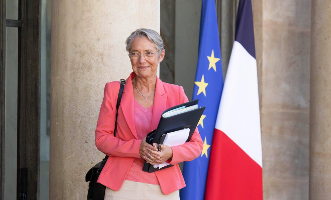 Elisabeth Borne avec drapeaux français et européen en arrière-plan.