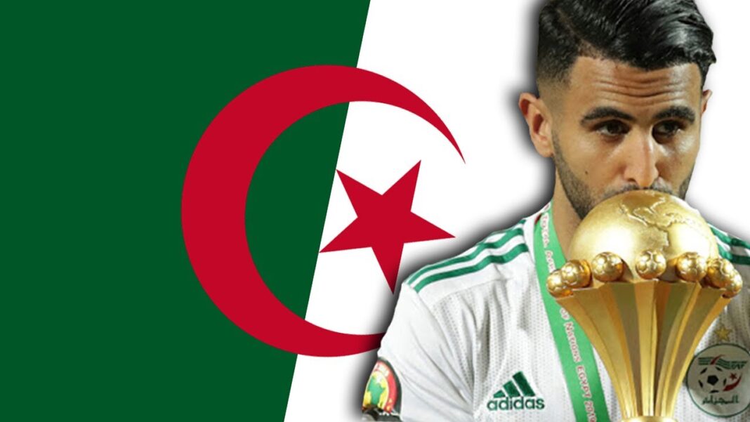 CAN 2025 : l’Algérie grandement menacée pour cette raison Footballeur algérien avec trophée et drapeau national.