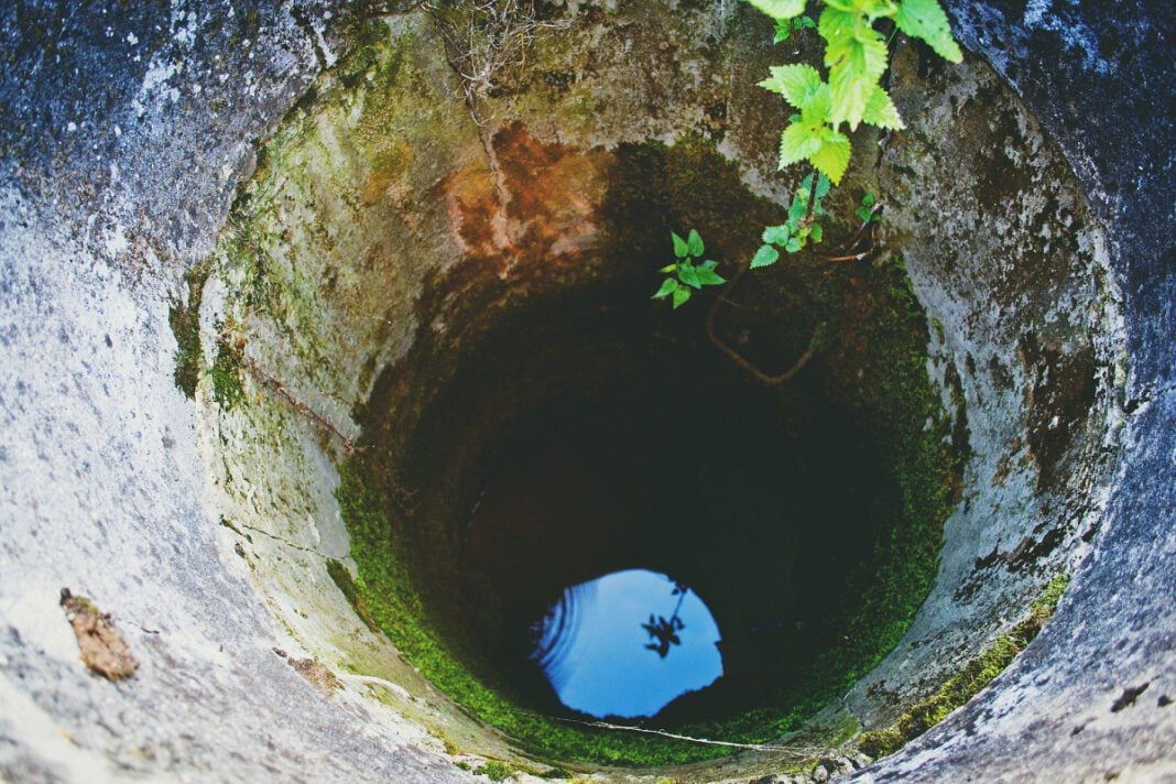 Puits abandonné en Algérie Puits profond avec de l'eau et végétation autour.