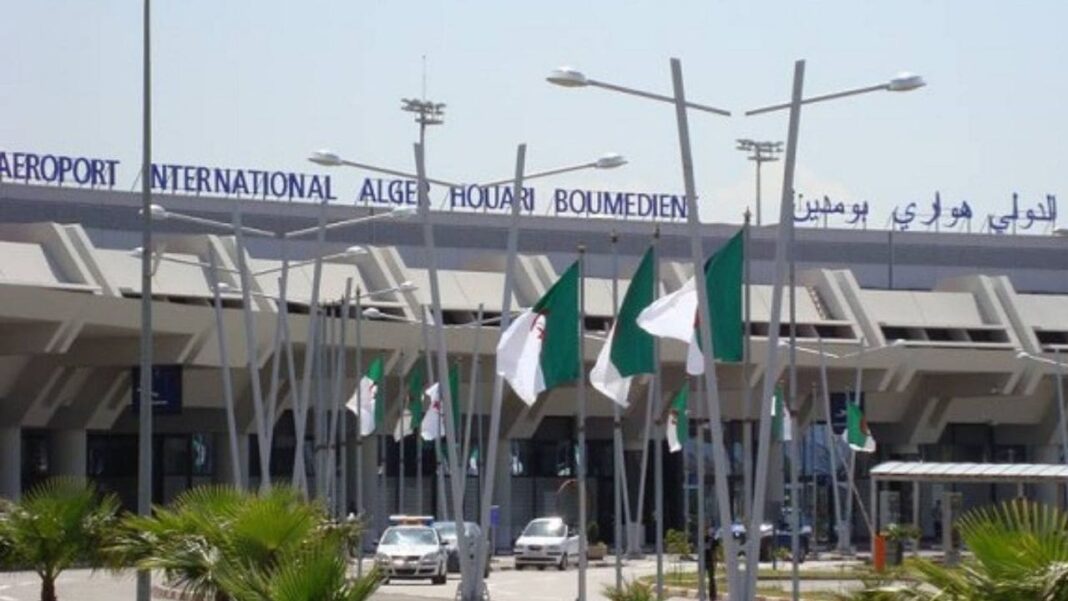 Vue extérieure de l'aéroport international d'Alger avec drapeaux et véhicules.