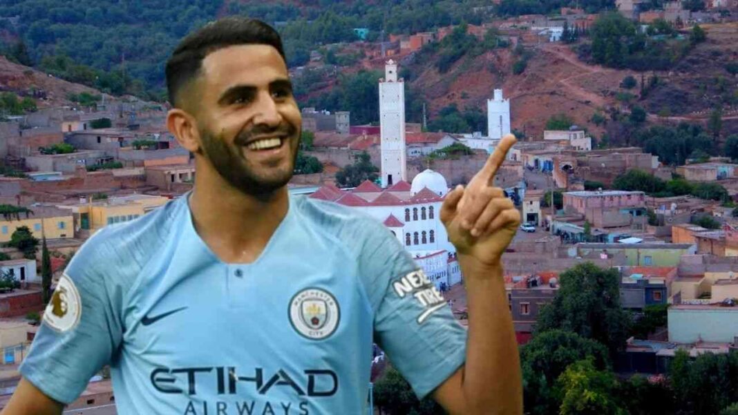 Man City : Mahrez remercie ses fans pour cette raison (vidéo) Riyad Mahrez souriant, pointant vers le ciel, avec la ville en arrière-plan.