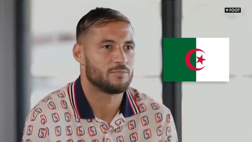 Belaïli explique son départ de Brest Belaïli lors d'une interview, avec drapeau algérien en arrière-plan.