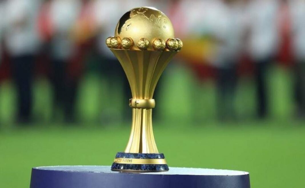 CAN 2025: Un joueur plaide pour une Co-organisation entre l’Algérie et le Maroc Trophée de la CAN 2025 sur un podium avec public en arrière-plan.