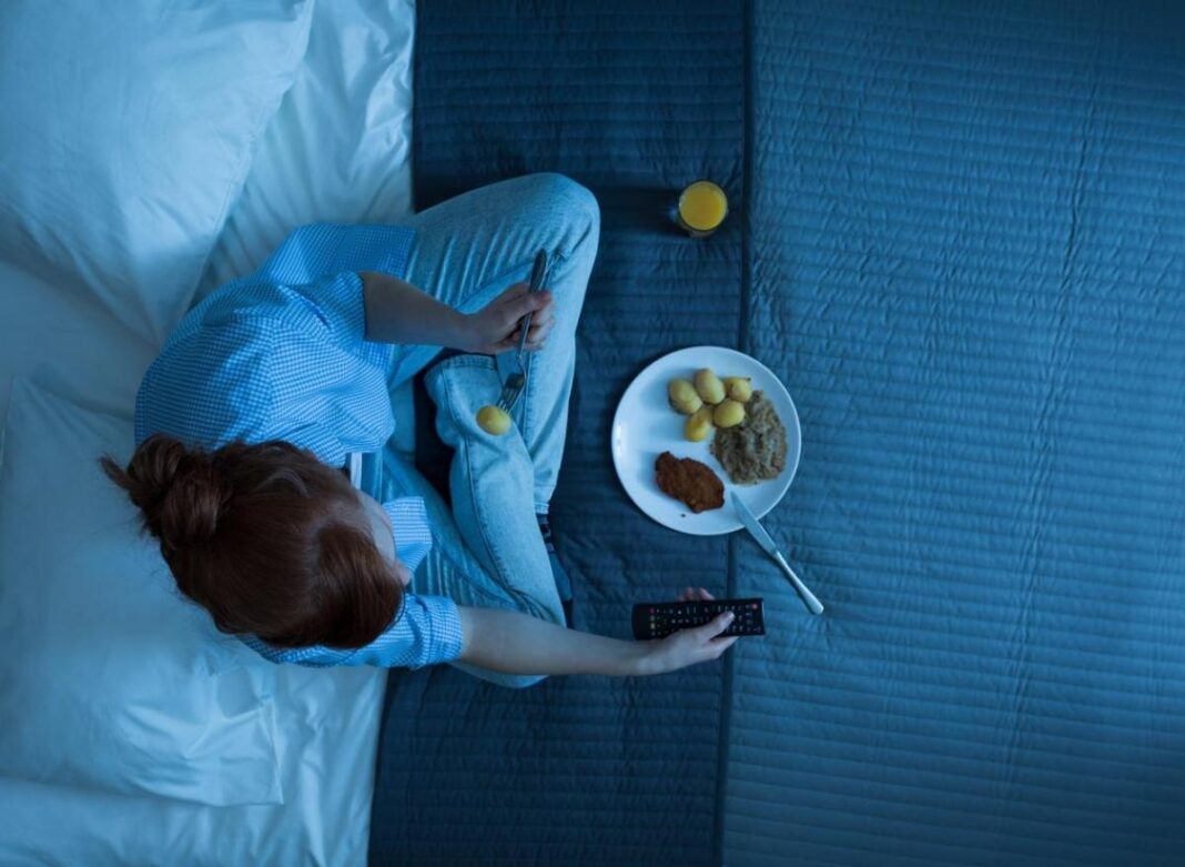 Femme regardant la télévision au lit Femme regardant la télévision dans la chambre avec un plateau de snacks.