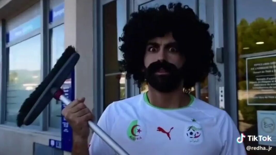 Coupe du monde : un humoriste binational trolle l’Algérie Humoriste avec perruque afro et canne, expression moqueuse.