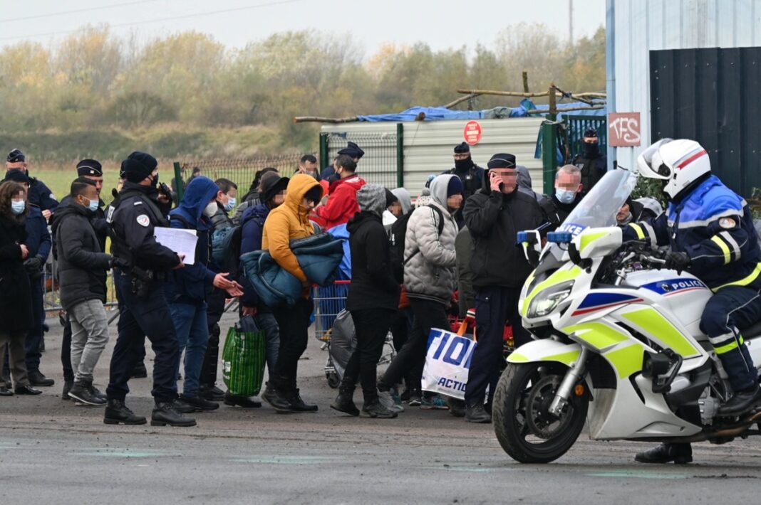 Flux de migrants en France Groupe de migrants faisant la queue avec des policiers et une moto de police.