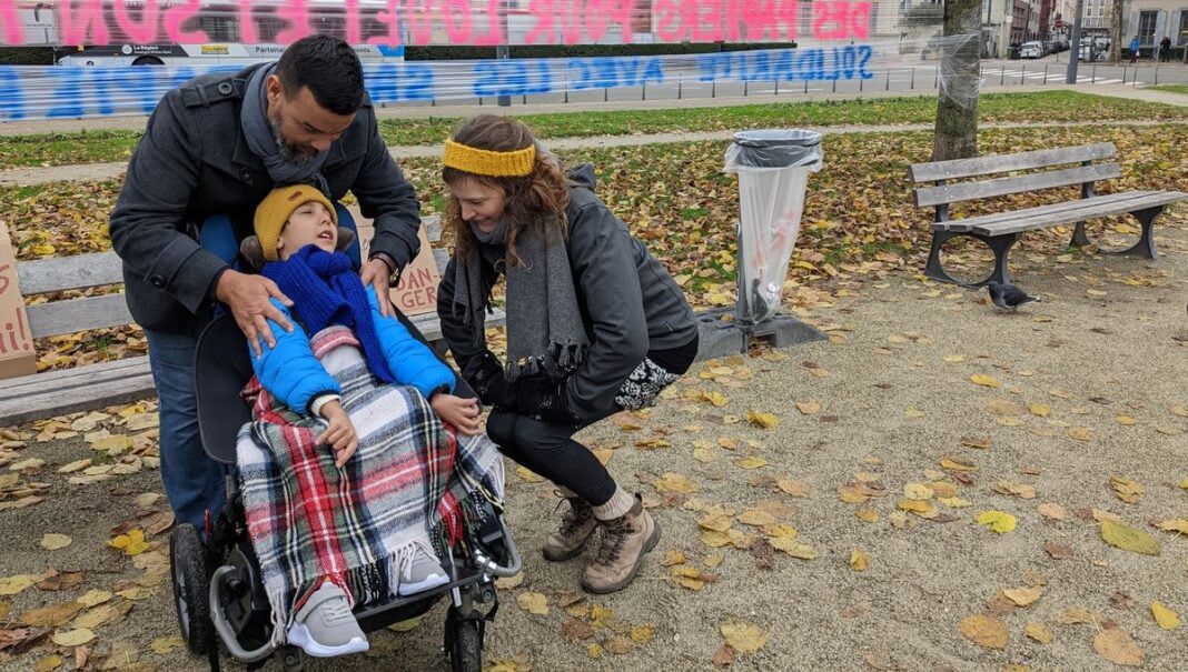 France: Menacé d’expulsion, un enfant algérien risque de mourir d’une maladie grave Enfant malade en fauteuil roulant entouré de deux adultes dans un parc.