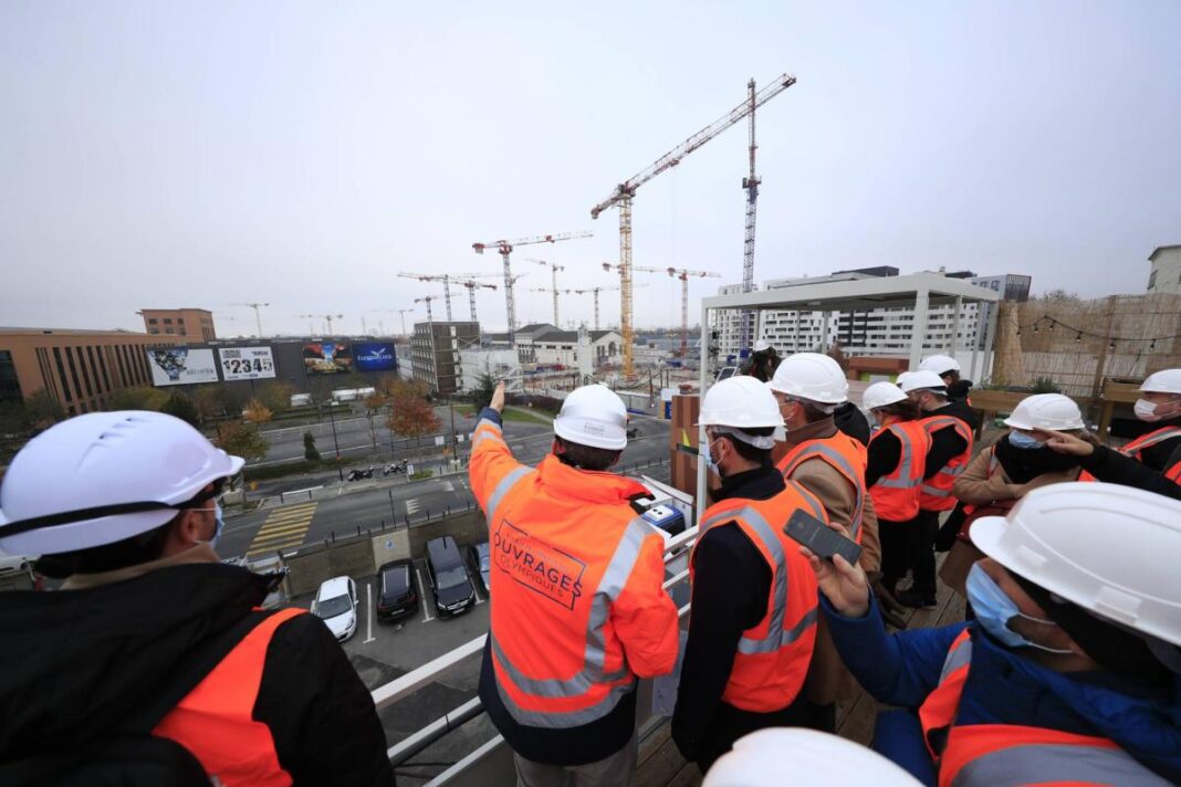 Travailleurs sur un chantier de construction pour Paris 2024 avec casques et vestes de sécurité.