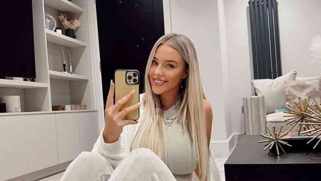 Incroyable : Taylor Ward, la femme de Mahrez, apparue avec une croix au cou. Femme souriante portant une croix au cou, prise selfie dans un intérieur moderne.