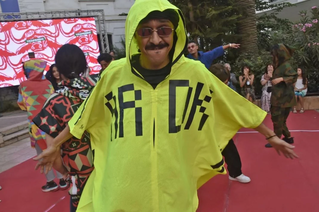 Culture : la tenue traditionnelle de l’est algérien en bonne voie pour faire partie des patrimoines de l’UNESCO Homme portant une cape jaune avec inscription, ambiance festive en plein air.