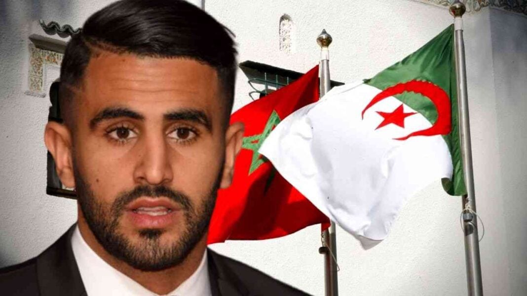 Riyad Mahrez avec drapeaux algérien et marocain Riyad Mahrez devant des drapeaux algérien et marocain dans une pièce.