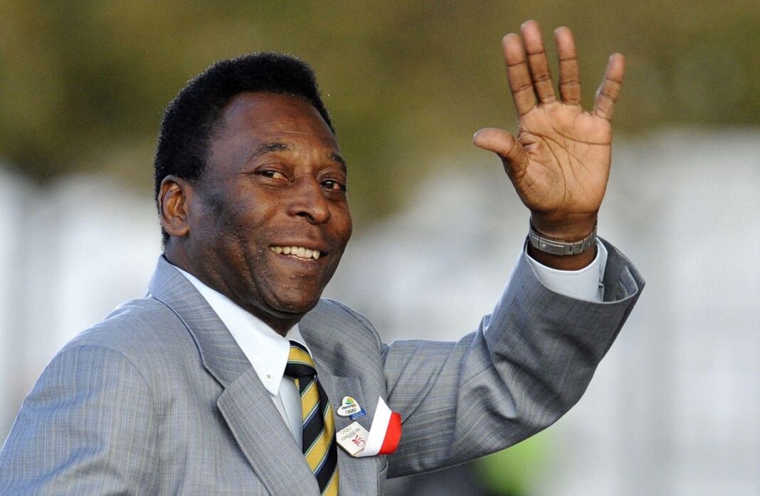 Le roi Pelé et l’Afrique : s’en est une histoire Pelé saluant avec un sourire, en costume gris et cravate.