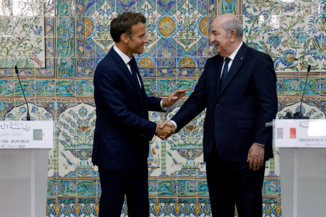 France-Algérie : la visite de Tebboune à Paris reportée Deux hommes en costume se serrent la main devant un décor marocain traditionnel.